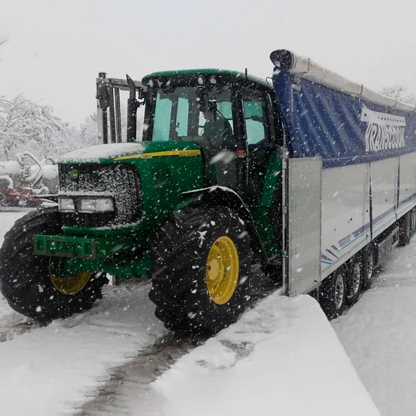 Tractor verde junto a un semirremolque de Transcosur en un día de nieve